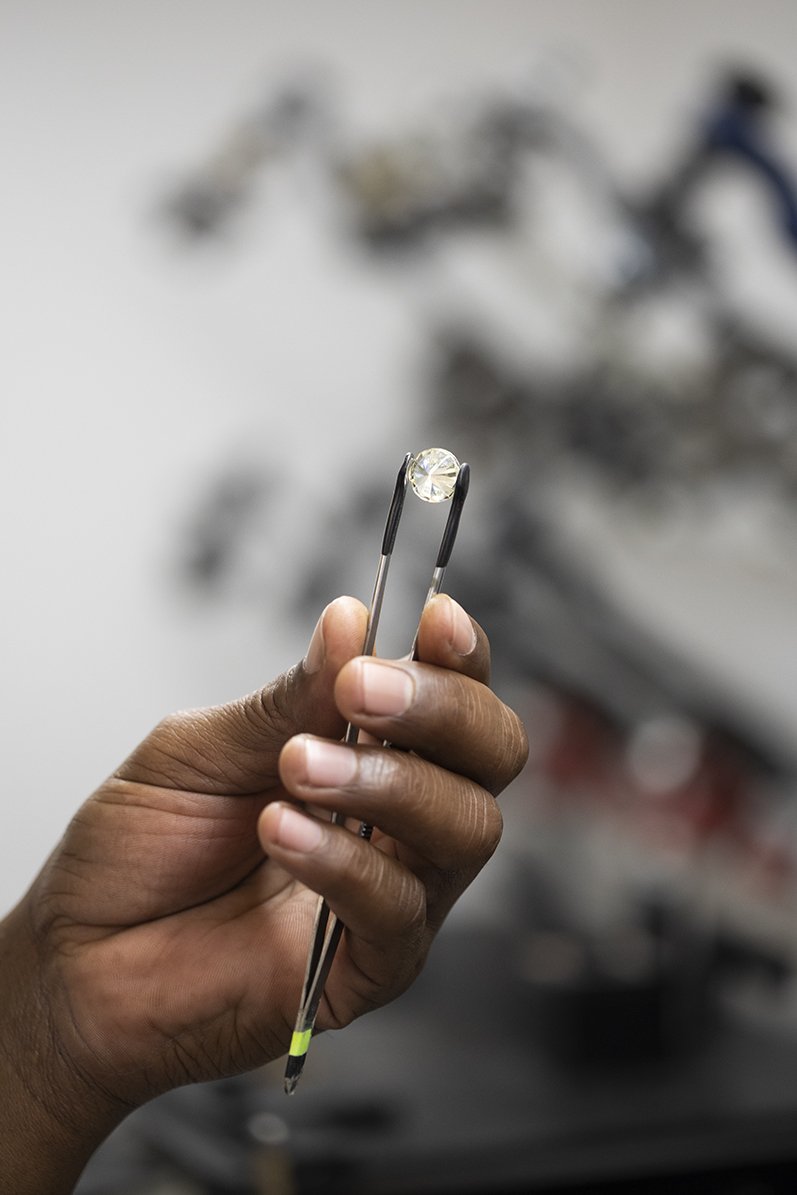 A polished diamond held with tweezers against a dark background