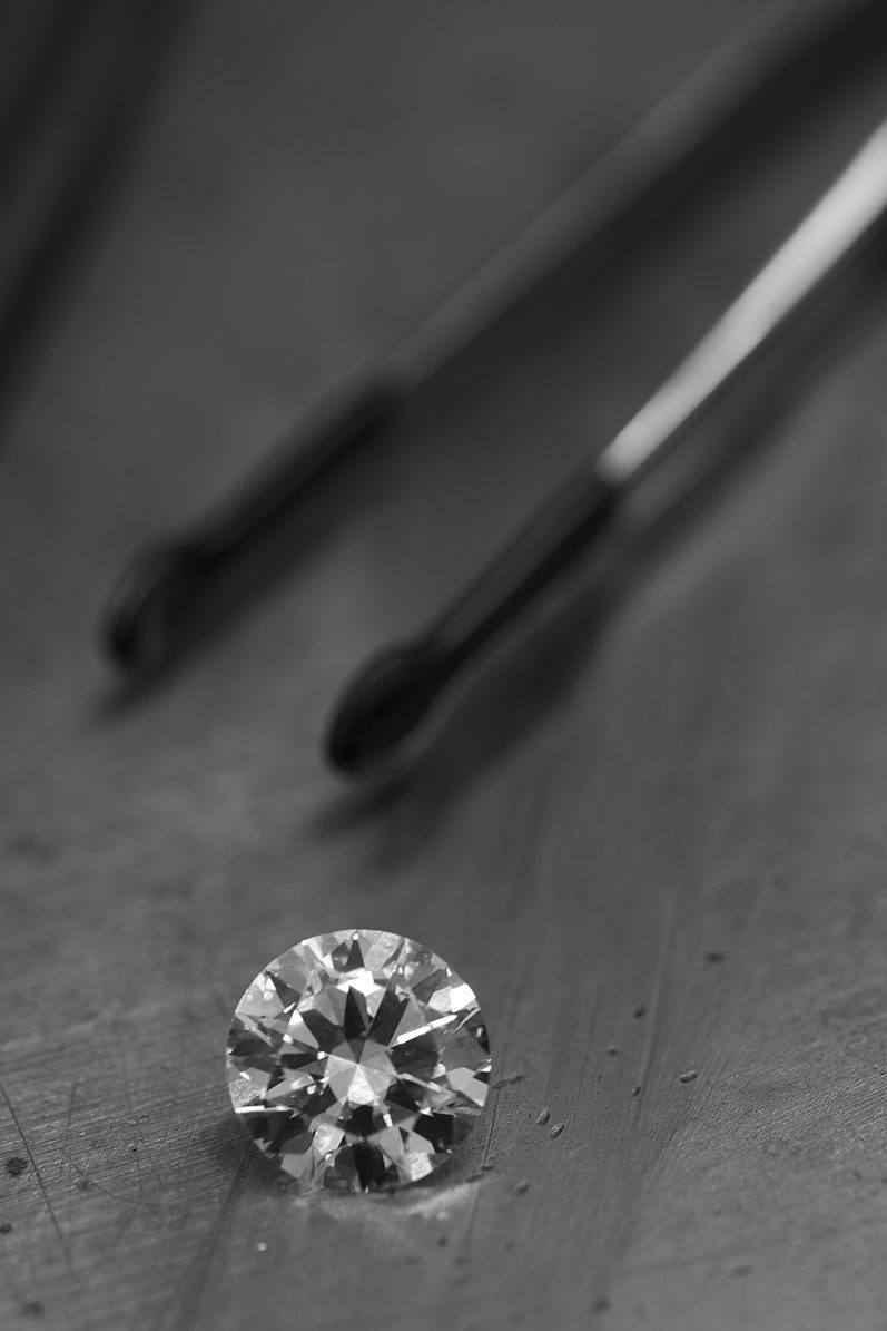 A polished round diamond beside a pair of tweezers